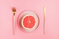 Half a grapefruit on a pink plate on a pastel background