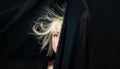 Half hidden portrait of blonde sexy woman fashion model, behind black cloth, whose hair is electrostatic charged and hanging on