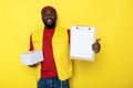 Half length of African man holding clipboard and delivery against yellow background Royalty Free Stock Photo