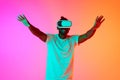 Half length image of african man play video games in VR-glasses vaving his hands over pink-orange background in neon. Royalty Free Stock Photo