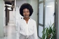 Half-length portrait of charming young purposeful African businesswoman with afro hair, wearing white shirt and gray