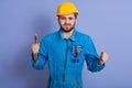 Half length portrait of confident worker holding wrench in hand, being very angry, clenching fists with anger, has serious facial