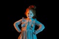 Half-length portrait of cute redheaded little girl wearing festive dress isolated over dark background in neon light