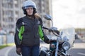 Half length portrait of female motorbiker in safety outfit standing near classic bike on urban streets