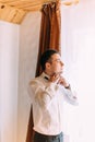 Half-length portrait of the groom tying the bow-tie while looking through the window. Royalty Free Stock Photo