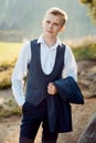 Half-length portrait of the handsome blond groom holding the jacket in the forest. Royalty Free Stock Photo