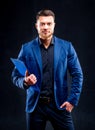 Half-length portrait of handsome young smiling man wearing dark shirt and blue suit holding blue folder Royalty Free Stock Photo