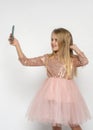 Little blonde girl with long hair in a beautiful pink dress posing making a selfie on a white background in the studio Royalty Free Stock Photo