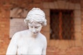 Half-length portrait of a Roman-style woman statue with a brick facade of a building with a barred window in the background. Royalty Free Stock Photo