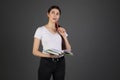 Half length portrait of thougtful dreamy woman holding red pen in hand near mouth, books in other hand Royalty Free Stock Photo