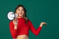 Half-length portrait of young beuatiful girl, student in casual style clothes with megaphone isolated on green studio