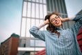 Half length portrait of young woman wearing blue shirt holding hands on the head while standing near office building. Successful Royalty Free Stock Photo