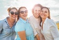 Half-length portraits of four cheerful smiling women in sunglasses embracing and looking at camera during outdoor walking with