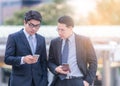 Half length of two young bearded modern businessman using smart phone handhold looking downward the screen - technology, business