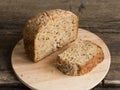 Half a loaf of homemade whole grain bread with various seeds and two slices on a wooden background