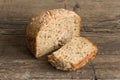 Half a loaf of homemade whole grain bread with various seeds and two slices on a wooden background