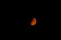 Half moon, orange from wildfire smoke, against a black sky