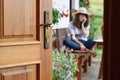 Half opened door into the beautiful summer terrace and blooming garden where young woman is sitting, relaxing and telephoning