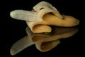 Half peeled banana on a black mirror surface with reflections isolated on black Royalty Free Stock Photo
