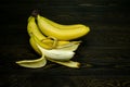 Half-peeled bright yellow juicy ripe banana and bundle of whole bananas on a coarse dark wooden background from boards Royalty Free Stock Photo