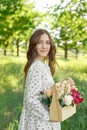 Half portrait of a charming positive woman dressed in long white summer dresses with a happy smile on the background of a green