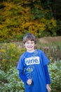 Half portrait of a smiling nine year old boy holding wild flowers outside in Autumn with colorful fall trees Royalty Free Stock Photo