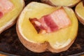 Potato half baked with bacon slice on baking sheet closeup