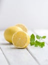 Half a ripe lemon and a mint branch on a white wooden table.