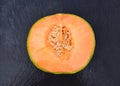 Half of ripe organic cantaloupe melon or muskmelon, mushmelon, rockmelon on a black stone background.