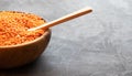 Half a round wooden bowl filled with red lentils with a wooden spoon. Dark background. Place for text