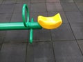 A half of seesaw with black floor background at the playground. Green and yellow seesaw.