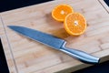 Half Sliced orange with knife on wooden cutting board.