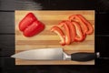 Half and sliced pieces of red sweet pepper in water drops and knife on a wooden board. Sliced bell peppers and a sharp Royalty Free Stock Photo