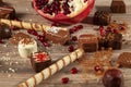Half sliced pomegranate with seeds scattered on wooden table covered with cookie sticks, assorted chocolates, Royalty Free Stock Photo