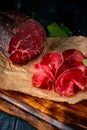 Half a smoked bresaola and cut pieces on a chopping Board Royalty Free Stock Photo