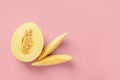 Half and two slices of yellow ripe honeydew melon over pastel pink background. Vegetarian, raw food diet and healthy eating Royalty Free Stock Photo