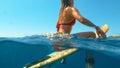 HALF UNDERWATER: Young woman sits on her surfboard and waits for big waves. Royalty Free Stock Photo