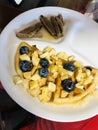 half waffle topped with blueberries and banana, sausage on side