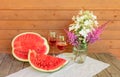 Half of watermelon, piece of watermelon, rose wine and hydrangea and astilbe flowers on aged wooden table