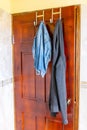Half worn clothes hanging on stainless steel/ chrome metal over the door hooks on inside bathroom/ bedroom/ room door.