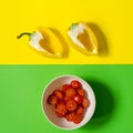 Half a yellow pepper on a yellow background and a plate with a red cherry tomato on a green background. Royalty Free Stock Photo