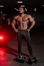 Halfnaked strong african american bodybuilder standing with sport equipment in dark modern gym.