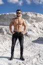 Halfnaked strong man in sunglasses standing in beautiful location. Bodybuilder posing