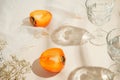 Halfs of persimmon fruits and two glasses of water on pastel background with white cloth and sunlit. Summer drinks and refreshment Royalty Free Stock Photo