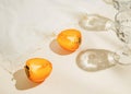 Halfs of persimmon fruits and two glasses of water on pastel background with white cloth and sunlit. Summer drinks and refreshment Royalty Free Stock Photo