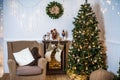 living room decorated for Christmas or New Year. Armchair with knitted plaid, pouf, fireplace, tree, beautiful interior in a Royalty Free Stock Photo