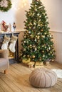 Living room decorated for Christmas or New Year. Armchair with knitted plaid, pouf, fireplace, tree, beautiful interior in a Royalty Free Stock Photo