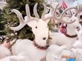 In the hall of the mall there is a plush deer standing next to a Christmas tree for sale