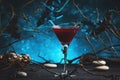 Halloween alcoholic cocktail bloody martini on scary dark blue background with twisted branches, bats, stones, pumpkin guards and Royalty Free Stock Photo