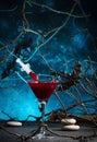 Halloween alcoholic cocktail bloody martini with syringe on scary dark blue background with twisted branches, bats, stones, Royalty Free Stock Photo